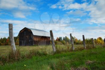 Wood fence in foreground with a little barn in a meadow during autumn season