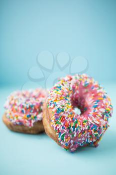 Two donuts with pink icing and candies on a blue pastel background