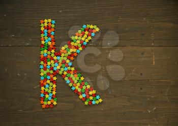 Letter K from alphabet made with star shape candy on a wooden background
