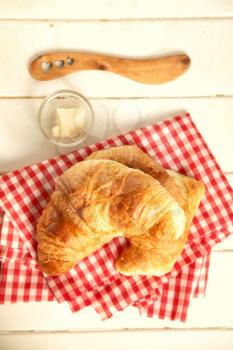 Fresh homemade croissant on red vichy clothe with butter and knife on a wooden background