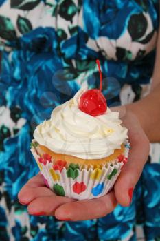 Women wearing blue flowered dress holding in hand a delicious vanilla cupcake with frosting and cherry on top