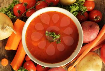 Vegetables soup surrounded by fresh vegetables on a wooden background