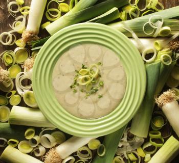 Top view of a leek soup in a green bowl surrounded by fresh leek.