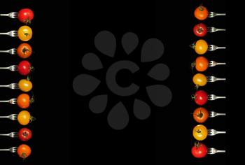 3 different kind of tomatoes on fork each side of the image with copy space on a black background