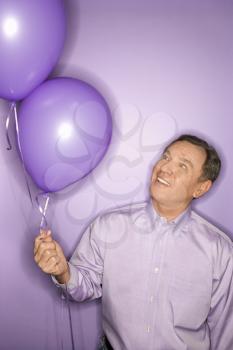 Smiling middle-aged Caucasian man on purple background holding purple balloons.