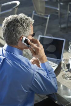 Royalty Free Photo of Businessman in a Suit Talking on a Cellphone and Looking at a Laptop