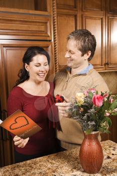 Caucasian man giving Caucasian woman card, present and flowers.