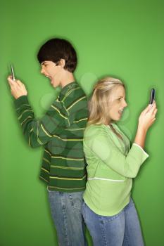 Royalty Free Photo of a Teen Boy and Girl Standing Back to Back Looking at Their Cellphones