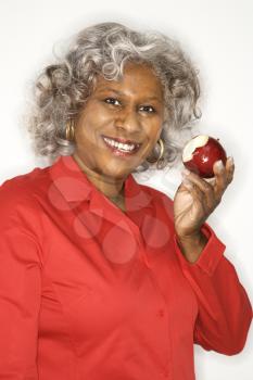 Mature adult African American female holding half eaten apple smiling.