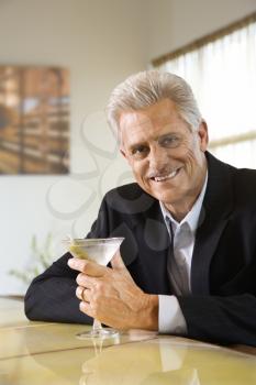Caucasian mature adult male sitting at bar with martini smiling.