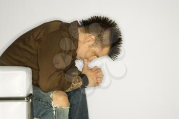 Royalty Free Photo of a Man With a Mohawk Sitting With Hands Clasped Together