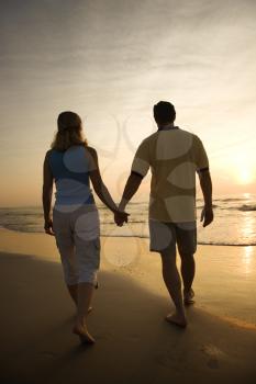 Royalty Free Photo of a Couple Holding Hands and Walking Down the Beach at Sunset