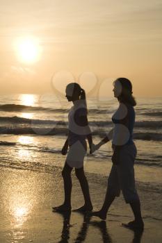 Royalty Free Photo of a Mother and Teenage Daughter Walking on the Beach at Sunset Holding Hands