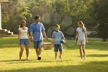 Royalty Free Photo of a Family of Four Walking in Park Carrying a Picnic Basket