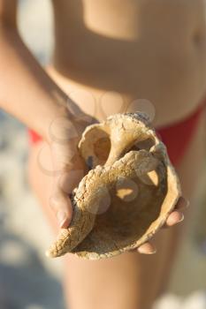 Caucasian mid-adult female in swimsuit holding seashell.