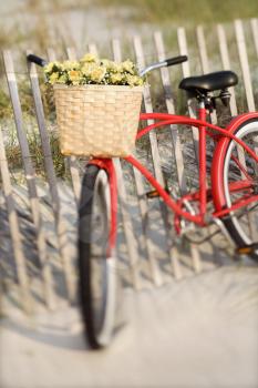 Royalty Free Photo of a Red Vintage Bicycle With a Basket and Flowers Leaning Against a Wooden Fence at a Beach