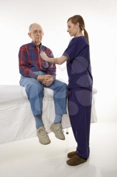 Royalty Free Photo of a female in scrubs listening to elderly Caucasian male's heart beat.