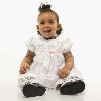 Portrait of African American infant girl sitting against white background.