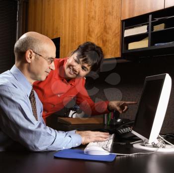 Royalty Free Photo of a Businessman and businesswoman in an Office Smiling Pointing at a Computer Monitor