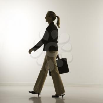 Silhouette of mid-adult Caucasian businesswoman walking and carrying briefcase.