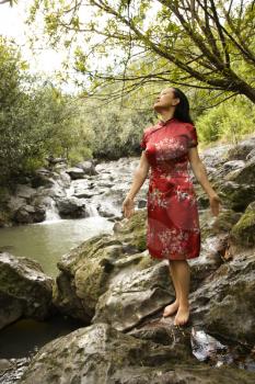 Royalty Free Photo of a Woman in Ethnic Attire Standing on Rock by a Creek in Maui, Hawaii