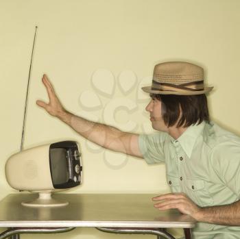 Royalty Free Photo of a Man Wearing a Hat Sitting at a 50's Retro Dinette Set Tapping an Old Television Set