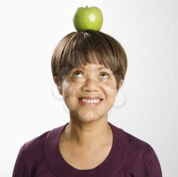 Portrait of African American middle-aged woman balancing green apple on head looking up and smiling.