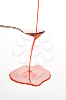 Royalty Free Photo of a Stream of Red Cough Syrup Overflowing Spoon Into a Puddle Below