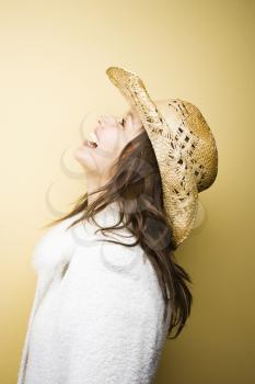 Profile of young adult Caucasian woman wearing cowboy hat leaning backwards laughing.