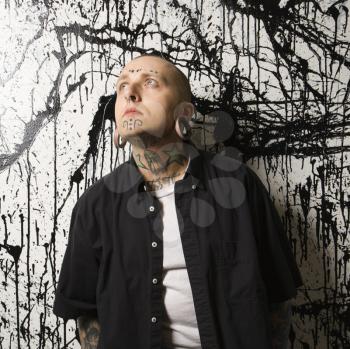 Royalty Free Photo of a Tattooed and Pierced Man Standing Against a Paint Splattered Background