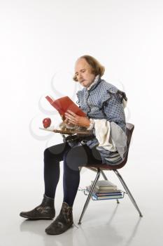 Royalty Free Photo of William Shakespeare in Period Clothing Sitting in a School Desk Reading a Book