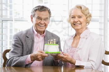 Mature Caucasian couple holding birthday cake looking at viewer.