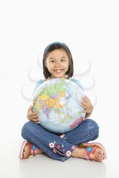 Asian girl sitting on floor holding Earth globe in her lap.