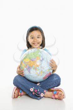 Asian girl sitting on floor holding Earth globe in her lap.