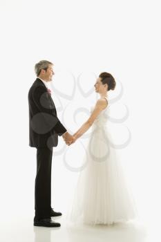 Portrait of Caucasian groom and Asian bride holding hands.