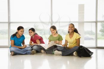 Preteen girls of mutiple ethnicities sitting together on floor with schoolwork smiling at viewer.