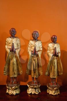 Three wooden statues of Buddhist disciples against orange wall.