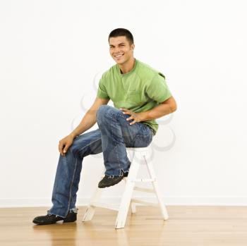 Attractive man sitting on stepladder in home smiling.