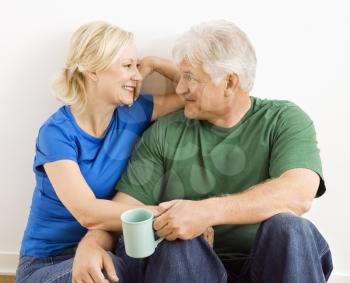 Middle-aged couple sitting together snuggling and drinking coffee.