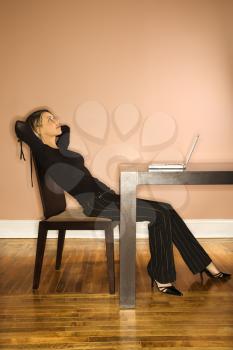 Attractive young businesswoman slouching in chair and looking up. A laptop is on the table in front of her. Vertical shot.