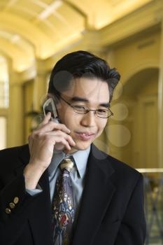 A young Asian businessman in an upscale hotel smiles with a mobile phone to his ear. Horizontal shot.