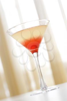 Mixed drink in a martini glass with red settling at the bottom. Vertical shot.
