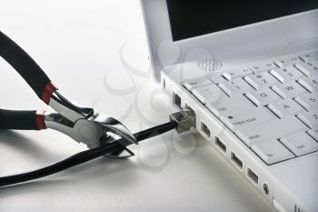 Wire cutters cutting a black Ethernet cable connected to a laptop. Horizontal shot.
