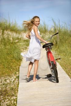 Young teen female smiles back as she walks her bike down a boardwalk. Vertical shot.