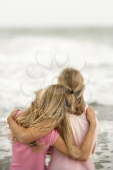 Rear view of a mother and daughter embracing at the beach. Vertical shot.