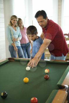 Man and boy playing pool with woman and girl in background. Vertically framed shot.