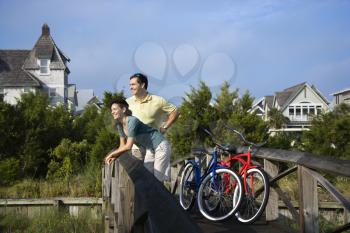 Man and woman leaning and relaxing on a bridge railing with their bikes. Horizontal shot.