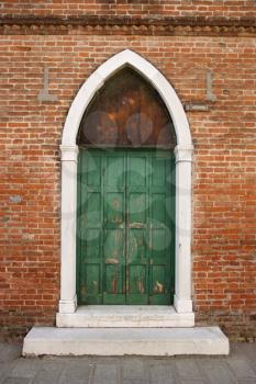 Weathered exterior doors in an arched doorway on a brick building in Venice, Italy. Vertical shot.