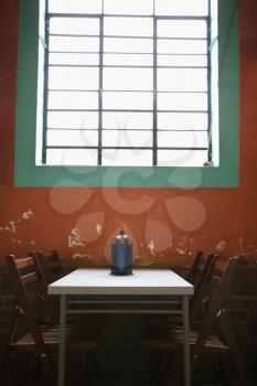 A simple table sitting under a window against a rustic wall. Vertical shot.
