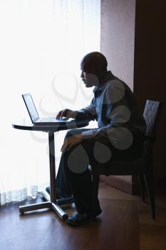 Portrait of African-American businessman sitting at a cafe table by a window with his laptop computer. Vertical shot.